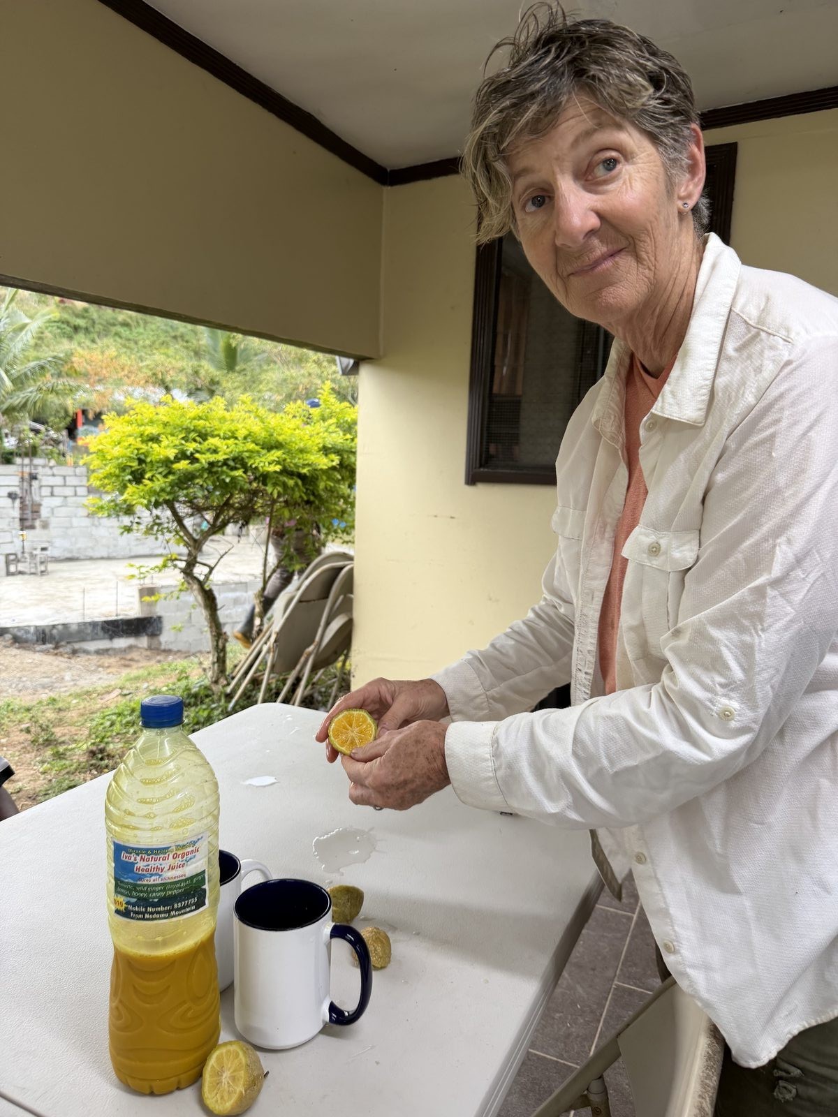 Whitney squeezing fresh citrus into a mug beside a bottle of Iva's Natural Organic Healthy Juice, found at the local street market in Fiji.